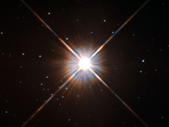 Shining brightly in this Hubble image is our closest stellar neighbour: Proxima Centauri. Proxima Centauri lies in the constellation of Centaurus (The Centaur), just over four light-years from Earth. Although it looks bright through the eye of Hubble, as you might expect from the nearest star to the Solar System, Proxima Centauri is not visible to the naked eye. Its average luminosity is very low, and it is quite small compared to other stars, at only about an eighth of the mass of the Sun. However, on occasion, its brightness increases. Proxima is what is known as a “flare star”, meaning that convection processes within the star’s body make it prone to random and dramatic changes in brightness. The convection processes not only trigger brilliant bursts of starlight but, combined with other factors, mean that Proxima Centauri is in for a very long life. Astronomers predict that this star will remain middle-aged — or a “main sequence” star in astronomical terms — for another four trillion years, some 300 times the age of the current Universe. These observations were taken using Hubble’s Wide Field and Planetary Camera 2 (WFPC2). Proxima Centauri is actually part of a triple star system — its two companions, Alpha Centauri A and B, lie out of frame. Although by cosmic standards it is a close neighbour, Proxima Centauri remains a point-like object even using Hubble’s eagle-eyed vision, hinting at the vast scale of the Universe around us.